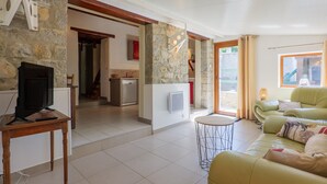 Un salon comprenant un téléviseur, un canapé, une petite table et un coin cuisine visible à travers une porte ouverte.