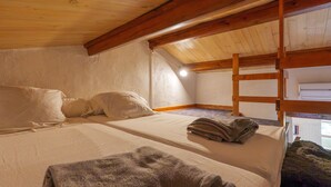 Une pièce avec un lit superposé, un lit simple, des poutres en bois, un plafond en pente et une fenêtre.