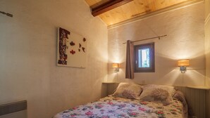 Une chambre à coucher avec une couvre-lit à motifs floraux, deux lampes de chevet, une fenêtre et une œuvre d’art accrochée au mur.