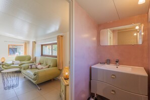 A room with a sofa, a small table, a mirror, and a sink.