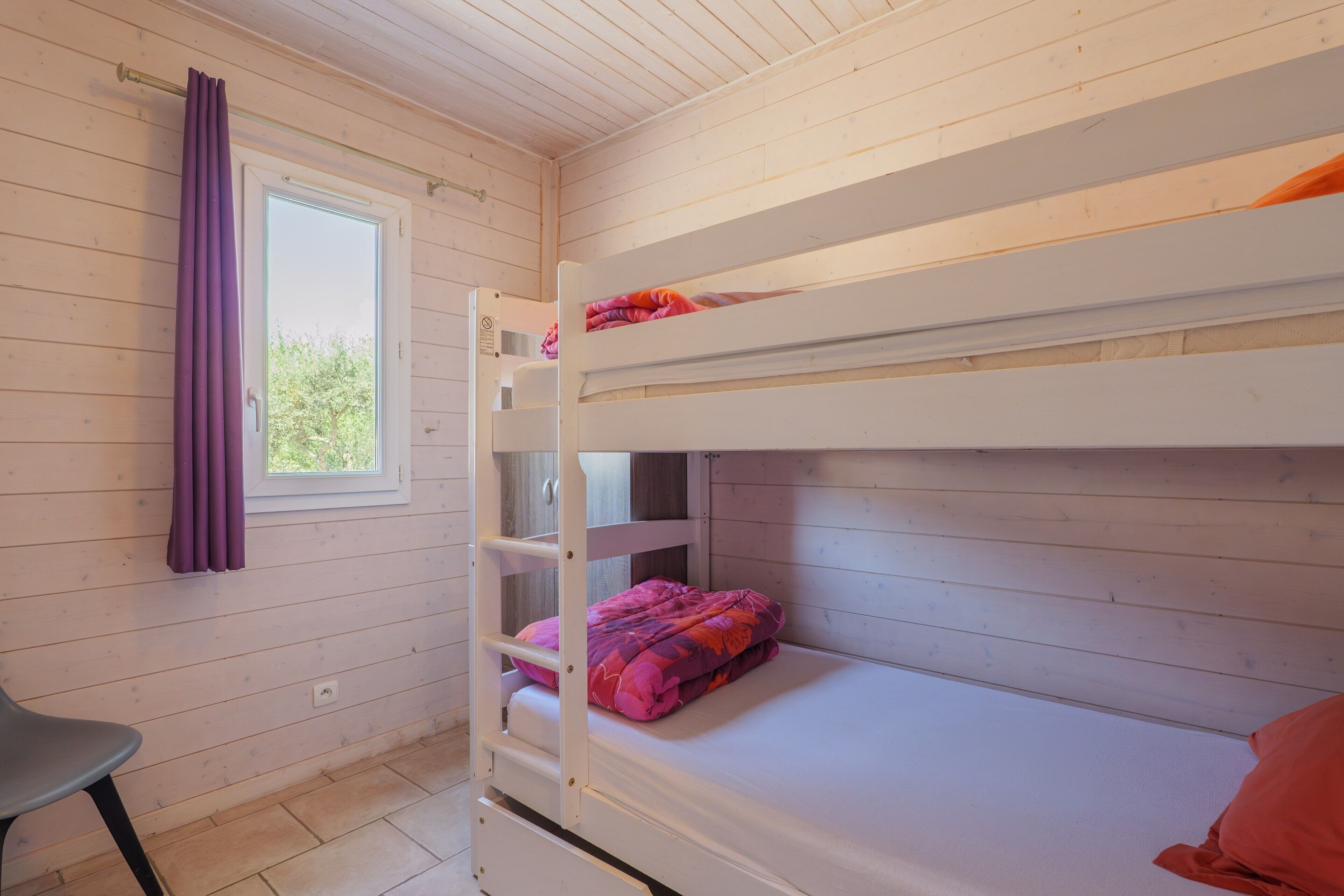 A bunk bed room with a window, a chair, and a door.