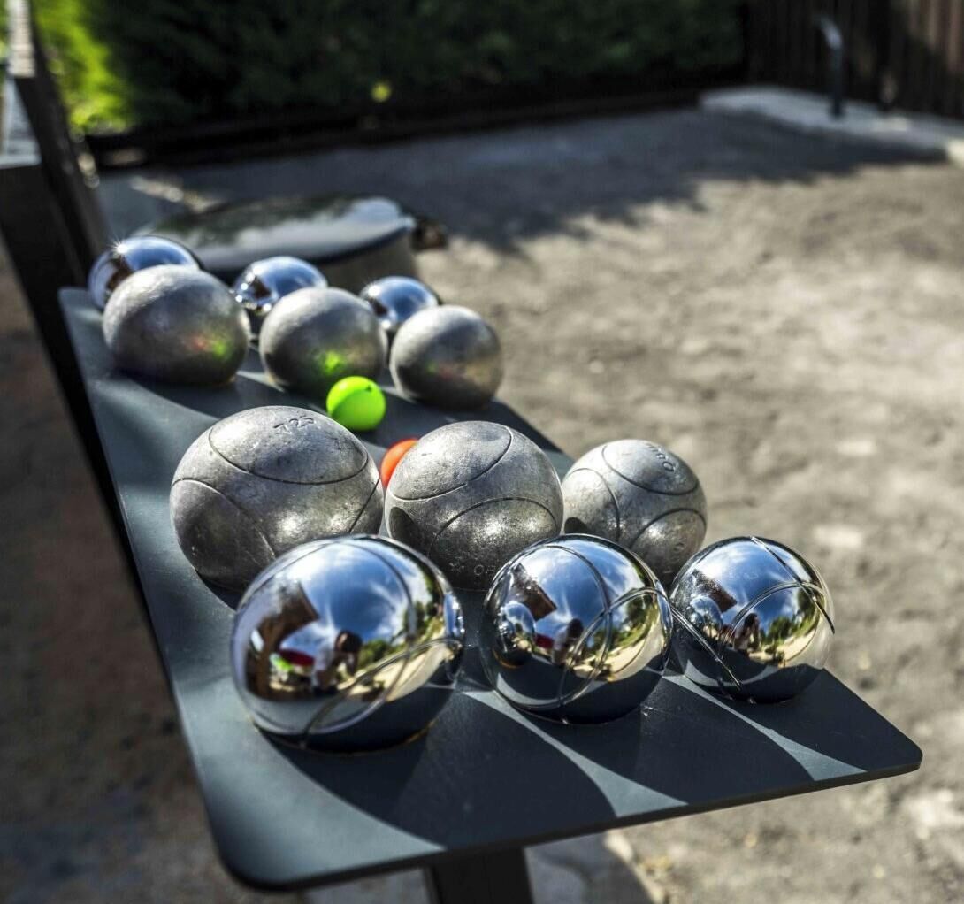 Une table avec plusieurs billes métalliques et une bille verte, probablement pour un jeu, en extérieur, avec un arrière-plan flou.