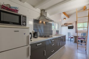 Une cuisine moderne équipée d’un four à micro-ondes, d’une cuisinière et d’une machine à café. On y trouve également un coin repas avec une table et des chaises, ainsi qu’un escalier menant à une mezzanine.
