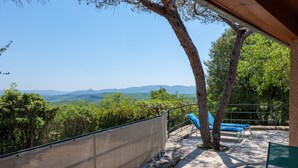 Une terrasse avec vue sur les montagnes, un mur en pierre et deux fauteuils bleus confortables.