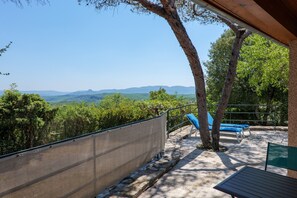 Eine Terrasse mit Blick auf Berge, eine Steinmauer und zwei blaue Liegestühle.