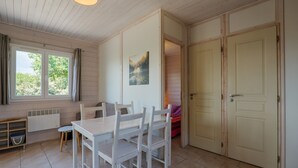 A room with a wooden table and chairs, a radiator, a window with curtains, and a door. - Gîte Romarin 1 – Village Holiday Rentals (Joyeuse)