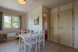 A room with a wooden table and chairs, a radiator, a window with curtains, and a door.