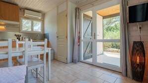 A kitchen with white cabinets, a dining table, and chairs, a sliding glass door to an outdoor area, and a flat-screen TV mounted on the wall. - Gîte Romarin 1 – Village Holiday Rentals (Joyeuse)