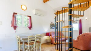 Ein Zimmer mit Esstisch, Stühlen, einer Couch, einer Treppe und einem Fenster mit Vorhängen.