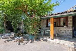 A stone building with a tiled roof, a wooden porch, and a table with chairs outside.