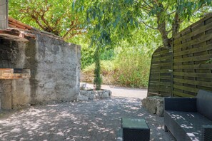 A courtyard with a stone wall, a small tree, a wooden fence, and outdoor furniture.