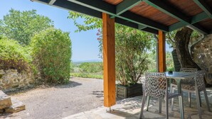 Un espace extérieur abrité, doté d’un sol en pierre, de piliers en bois et offrant une vue sur la verdure et les collines lointaines.
