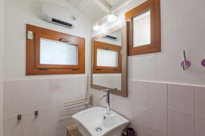 A bathroom with a white sink, a mirror, and a window with frosted glass.