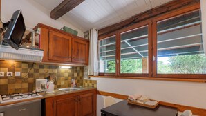 Une cuisine avec des meubles en bois, une cuisinière à gaz, une machine à café et une fenêtre avec des stores.
