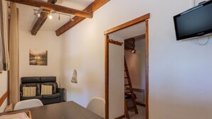 Une pièce avec une table en bois, un canapé en cuir noir, un téléviseur fixé au mur et une échelle appuyée contre le mur.