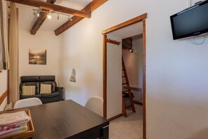 Una habitación con una mesa de madera, un sofá de cuero negro, un televisor montado en la pared y una escalera apoyada contra la pared.