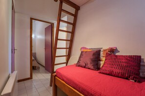 A bedroom with a wooden ladder, a red bedspread, and multiple pillows.