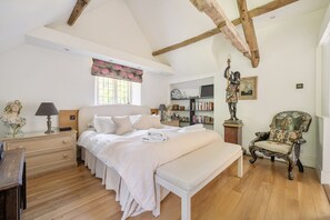 Een slaapkamer met een groot bed, een houten bankje, een stoel, een boekenkast en een beeld.