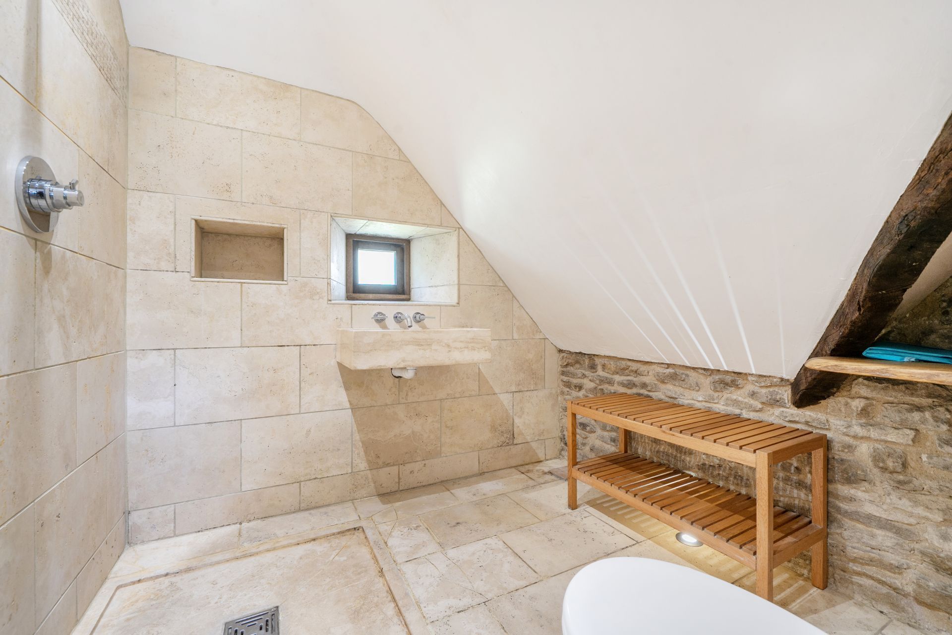 Une salle de bain avec un mur en pierre, une étagère en bois et une baignoire blanche.