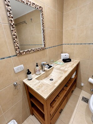 Een badkamer met een behanggekleurde betegelde muur, een houten wastafelmeubel met een wastafel, een spiegel met een mozaïek lijst, en een toilet.