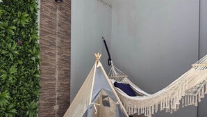 A hammock and a tent in a room with tiled flooring and a green plant wall.
