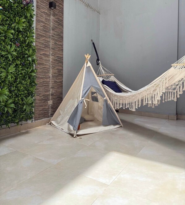 Een hangmat en een tent in een kamer met betegelde vloer en een groene plantenwand.