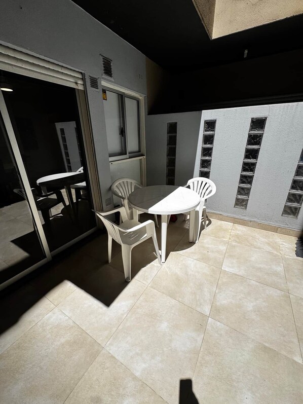 An outdoor patio with a table and chairs, a sliding door, and a tiled floor.