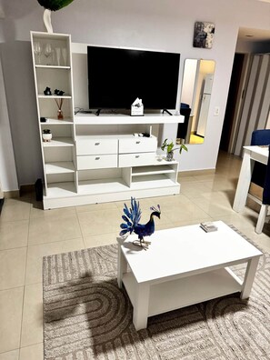 A modern living room with a flat-screen TV, white entertainment unit, and a decorative peacock statue on a coffee table.