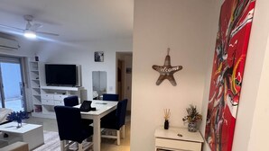 A modern living room with a TV, dining table, chairs, and a decorative starfish sign.