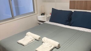 A neatly made bed with pillows, a bedside table with a lamp, and a window with blinds.