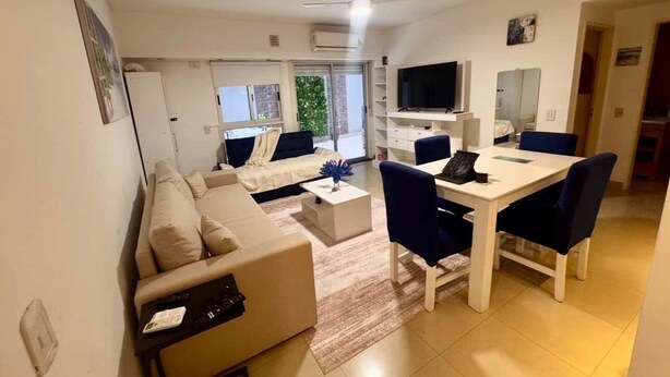 A modern living room with a sofa, coffee table, TV, and dining area.