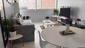 Una sala moderna con un sofá, una mesa de comedor con sillas, un televisor y un ventilador de techo.