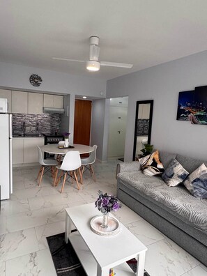 Ein modernes Wohnzimmer mit einem grauen Sofa, einem weißen Couchtisch und einem Essbereich mit einem weißen Tisch und Stühlen.