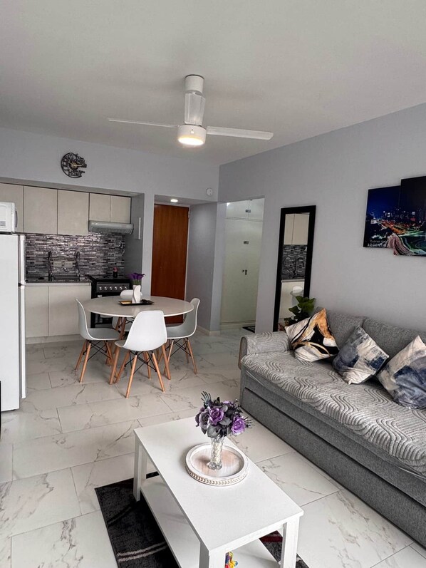 A modern living room with a grey sofa, a white coffee table, and a dining area with a white table and chairs.