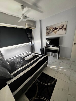 Ein Schlafzimmer mit einem Bett, Deckenventilator, Klimaanlage, Fernseher und einem Bild an der Wand.