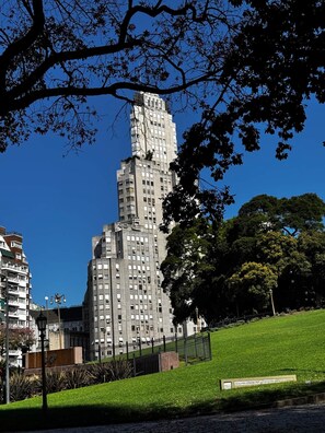 A tall, multi-story building with a distinctive top section, surrounded by a grassy area and trees.