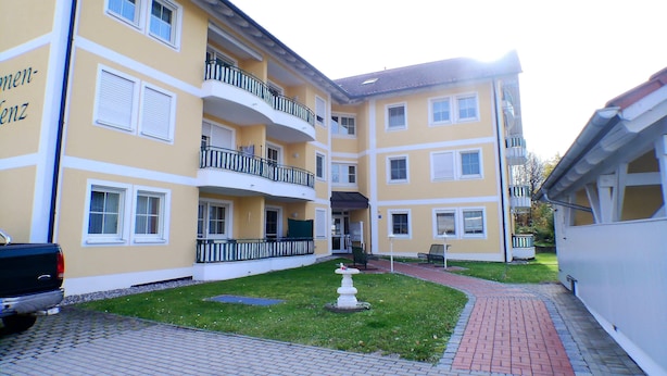 A multi-story residential building with balconies, a paved courtyard, and a small garden area.