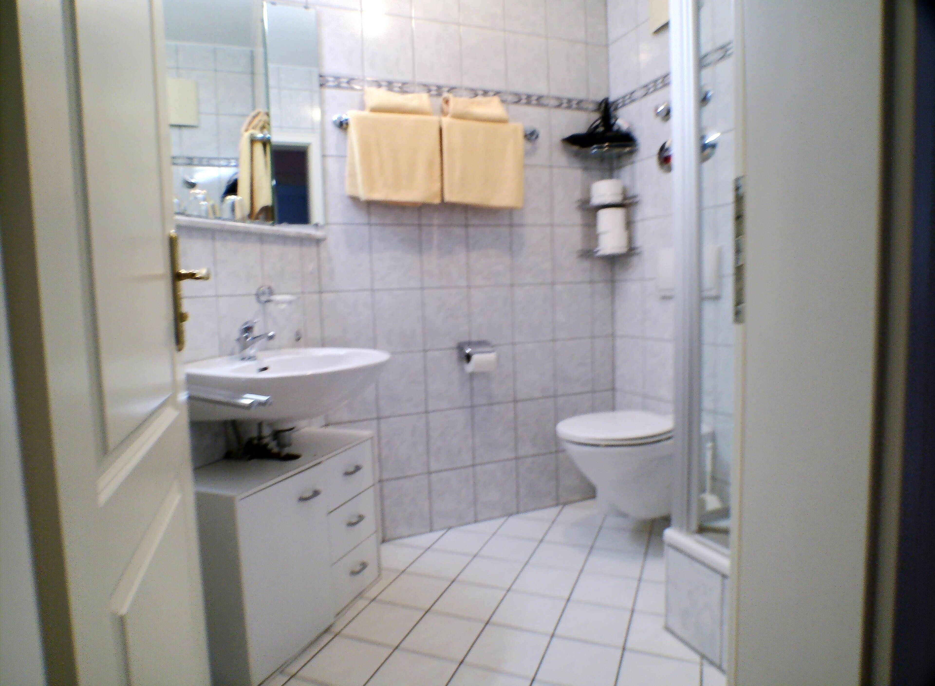 A bathroom with a sink, toilet, and shower. There are towels hanging on the wall.