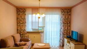 A living room with a sofa, a dining table, a TV on a cabinet, and a window with curtains.
