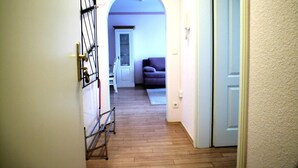A hallway with wooden flooring, a white door on the right, and a purple couch in the background.