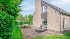 A two-story house with a brick exterior, a paved patio, and a small garden area. - Charming Villa Near the sea and Forest (De Koog)
