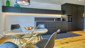 A modern kitchen with dark cabinetry, a glass-top dining table, and a built-in oven. - Apartment with a view of the surrounding mountains (Pfalzen)