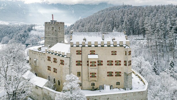 A historic castle with a prominent tower, surrounded by snow-covered trees and mountains in the background. - Apartment with a view of the surrounding mountains (Pfalzen)
