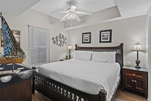 Quarto com cama, mesas de cabeceira, ventilador de teto e quadros na parede.