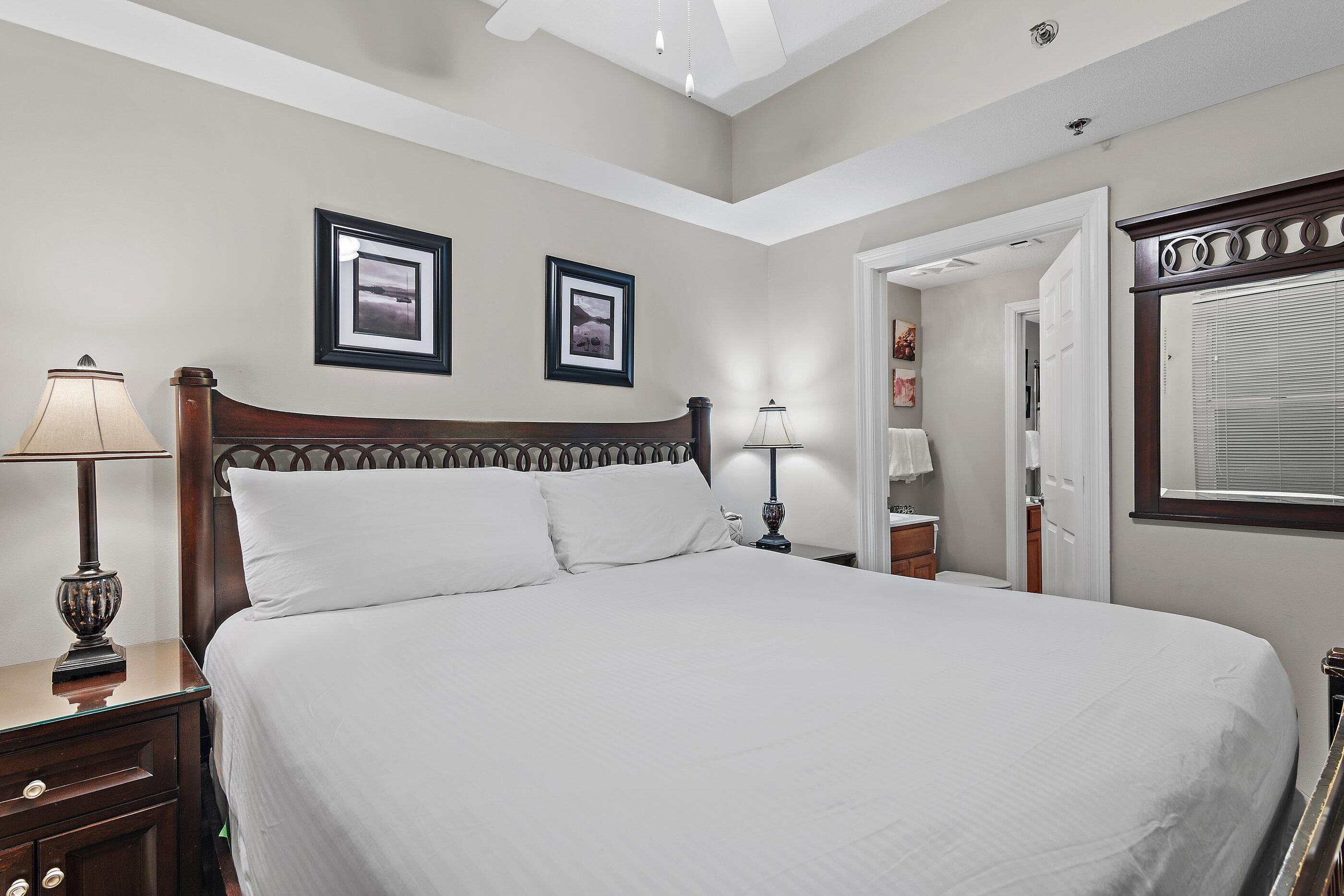 A neatly made bed with white linens, a wooden headboard, and two framed pictures on the wall.