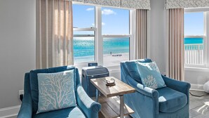A room with two blue armchairs, a small wooden table, and large windows offering a view of the beach. - Cabana Club C408- Sugar Sand Shores (Destin)