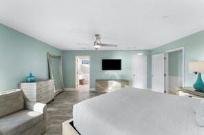 Une chambre à coucher avec un grand lit, une commode, un téléviseur fixé au mur et un ventilateur de plafond.