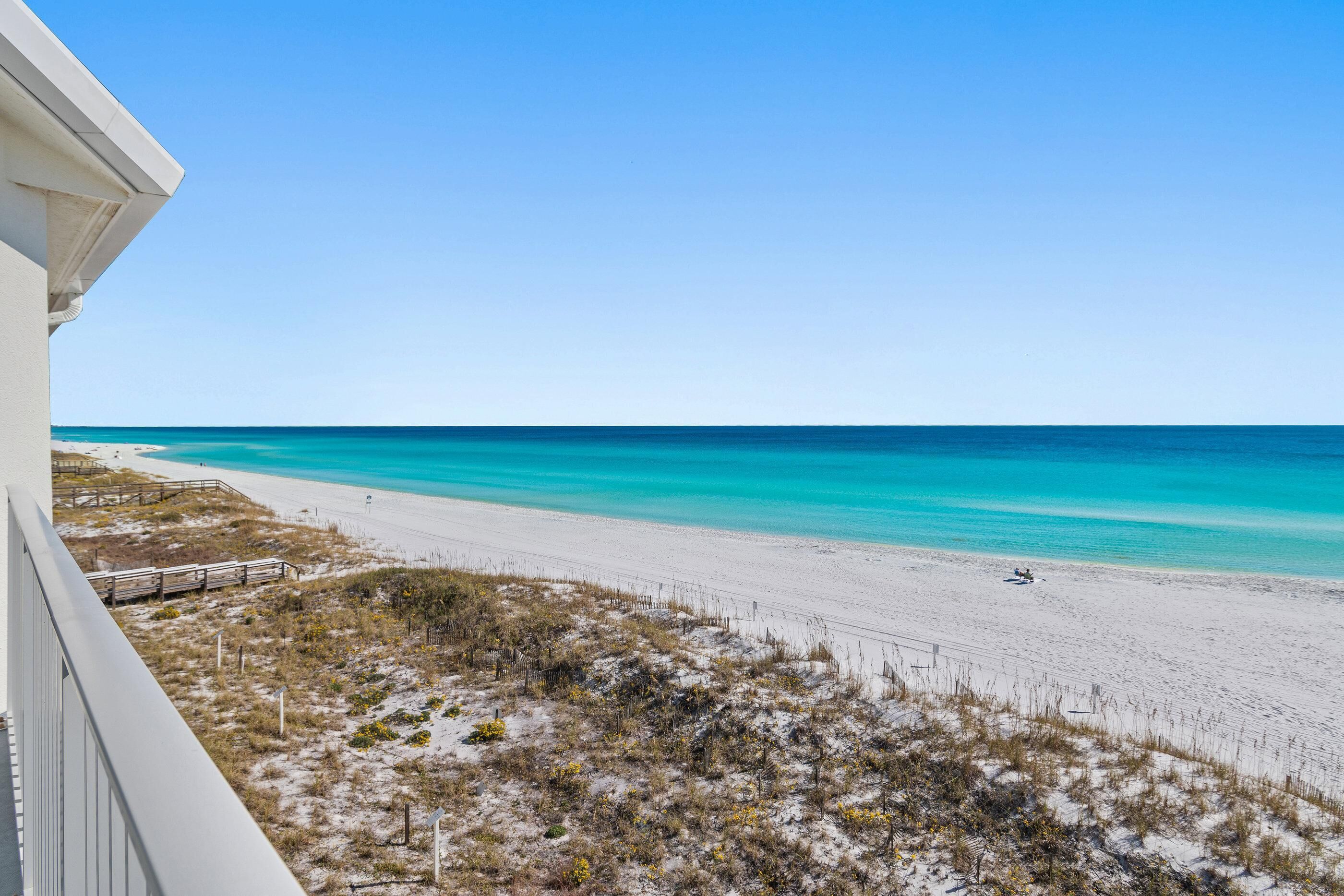 A beach with clear turquoise water, a sandy shore, and sparse vegetation.