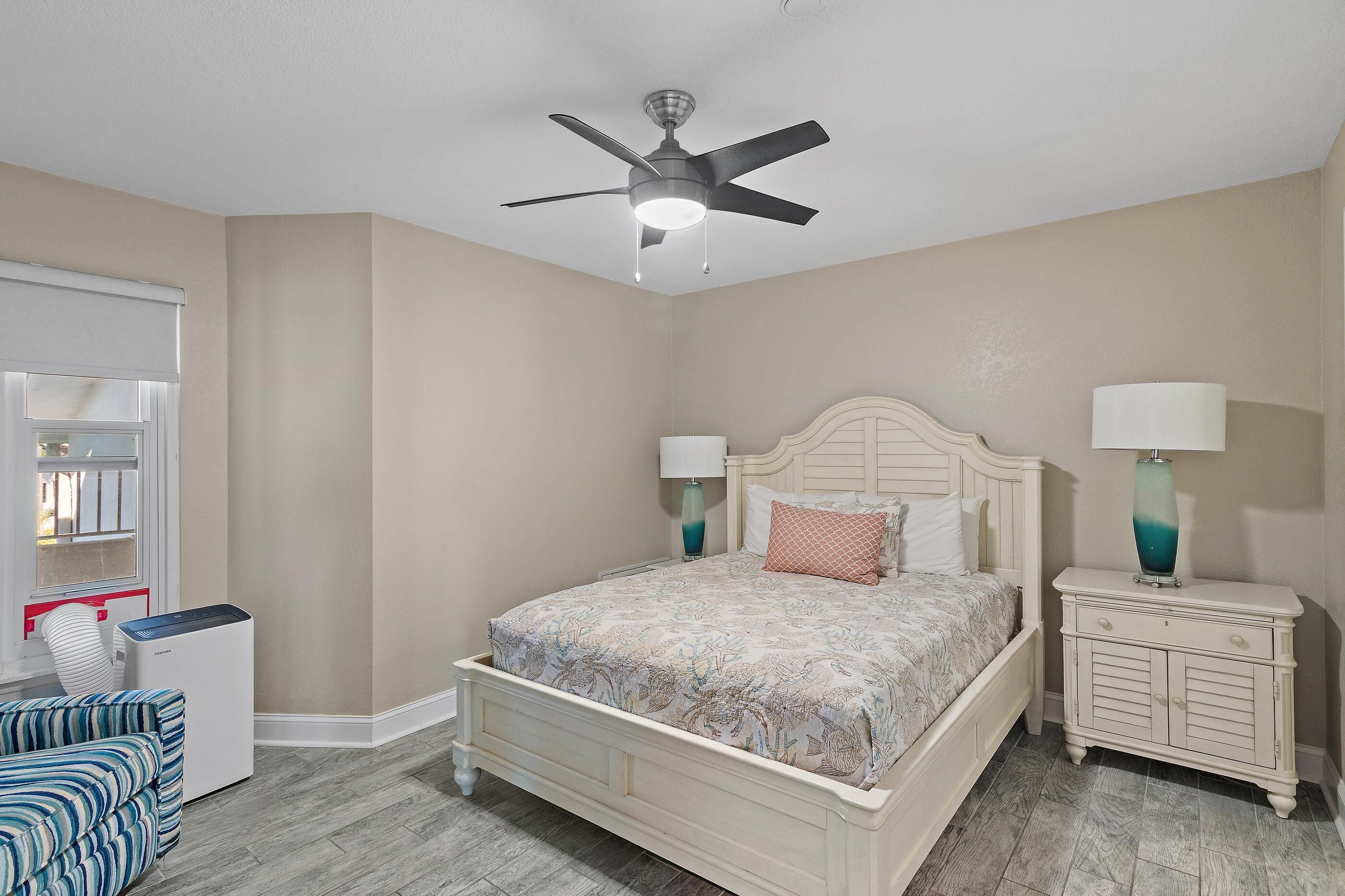 A bedroom with a bed, nightstands, a ceiling fan, a dresser, and a window with blinds.