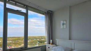 A bedroom with a bed, a window with a view of the countryside, a radiator, and a bedside table with a lamp. - 2 Person Apartment With sea View (De Koog)